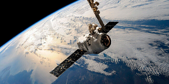 Ein Satellit im Orbit der Erde im Vordergrund, im Hintergrund sieht man einen Ausschnitt der Erde mit Wolken und Meer