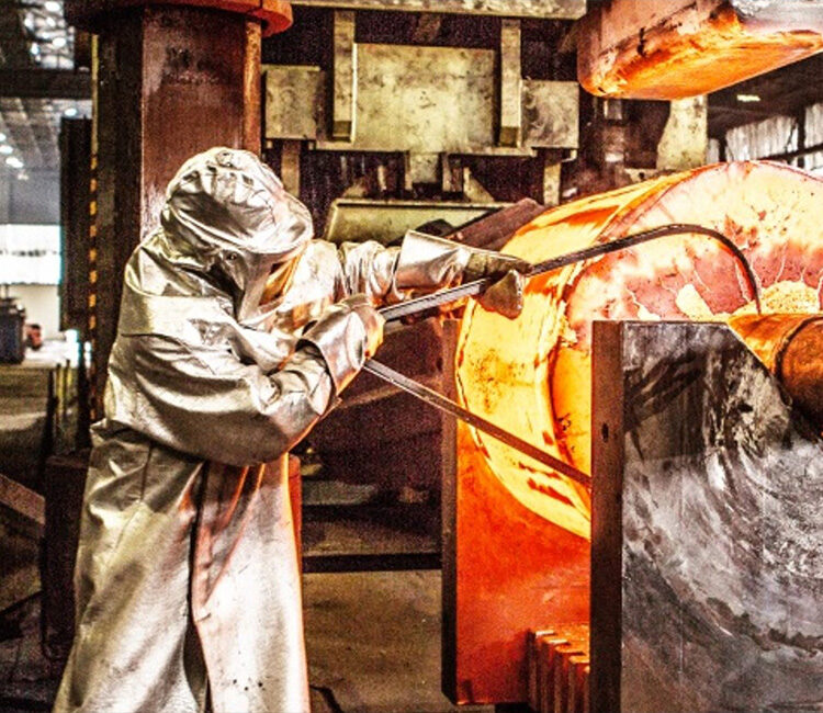 Ein Stahlarbeiter in Schutzkleidung an einer glühenden Metallwalze