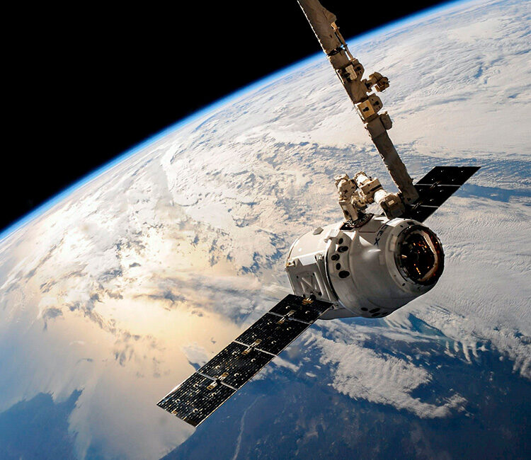 Ein Satellit im Orbit der Erde im Vordergrund, im Hintergrund sieht man einen Ausschnitt der Erde mit Wolken und Meer